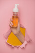 A woman's hand shows a bottle of cleansing foam through a hole in a paper background.