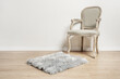 an unvarnished light wooden armchair with a gray upholstered seat, a gray shag rug in a room with white walls and light parquet floors