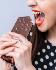 Wall Mural - Young woman eating chocolate bar on gray background