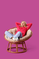 Sticker - Beautiful young woman in stylish hoodie sitting on armchair against purple background