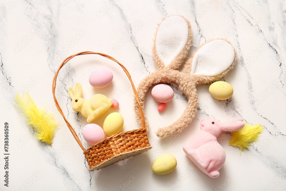 Bunny ears with Easter eggs and wicker basket on white marble background