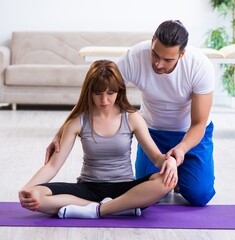 Wall Mural - Male physiotherapist doing exercises with injured woman on floor