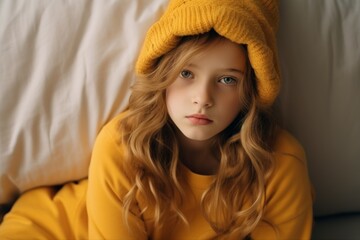 Portrait of a beautiful little girl in a yellow hat on the bed