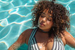 A beautiful young latin American woman plus size in a striped swimsuit in the pool. body positive, enjoying the moment.