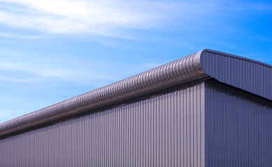 Wall Mural - Curve corrugated metal roof eaves with gray aluminium steel wall of modern industrial rental warehouse building against blue sky background, low angle and perspective side view