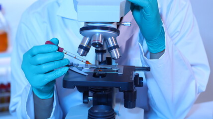 Scientists are doing research in a science lab. A medical chemist in a white coat, gloves and goggles looks at a glass tube. Compare two different liquid samples. and discuss future experiments.