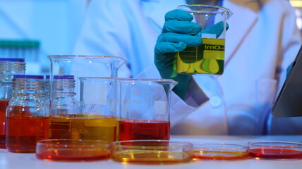 Scientists are doing research in a science lab. A medical chemist in a white coat, gloves and goggles looks at a glass tube. Compare two different liquid samples. and discuss future experiments.