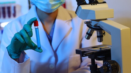 Scientists are doing research in a science lab. A medical chemist in a white coat, gloves and goggles looks at a glass tube. Compare two different liquid samples. and discuss future experiments.