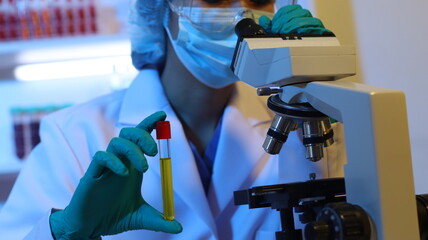 Scientists are doing research in a science lab. A medical chemist in a white coat, gloves and goggles looks at a glass tube. Compare two different liquid samples. and discuss future experiments.