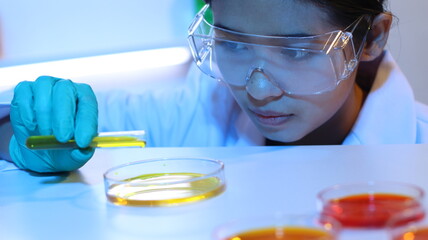 Scientists are doing research in a science lab. A medical chemist in a white coat, gloves and goggles looks at a glass tube. Compare two different liquid samples. and discuss future experiments.