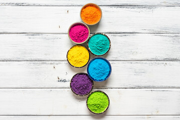 Wall Mural - Colorful Holi powders in bowls on a white wooden table. Vertical border. Top view, flat lay.