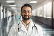 © Stock 4 You - Headshot portrait of smiling mature indian doctor wearing white coat, stethoscope looking at camera standing in hospital corridor. Therapist or general practitioner, medical staff, clinic presentation