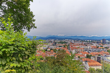 Wall Mural - Aerial view of City of Ljubljana seen from Sance castle hill with mountain panorama in the background on a cloudy summer day. Photo taken August 9th, 2023, Ljubljana, Slovenia.