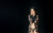© SergeiPh - A young sexy woman in black lingerie stands alone in a dark room.
