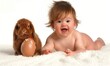 Cute, funny easter holiday portrait representing a naked toddler with open mouth and happy face close to an adorable baby angora floppy-eared red rabbit watching over a huge egg isolated on white