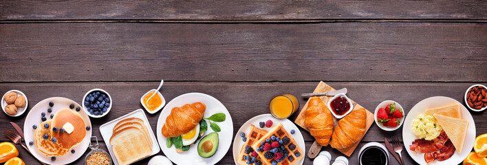 Leinwandbilder - Breakfast or brunch bottom border on a dark wood banner background. Top down view. Assorted sweet and savory food items.