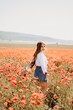 © svetograph - Happy woman in a poppy field in a white shirt and denim skirt with a wreath of poppies on her head posing and enjoying the poppy field.