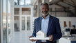 © Studio Nova - confident middle-aged man in a blue suit holding a model house, standing in a modern home interior.
