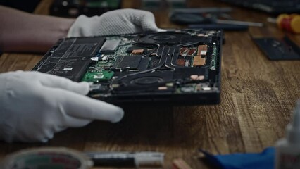 The person is holding a circuit component, specifically a motherboard, on a wooden table.