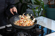 Close up of Chef cook hands cooking and toss roasted vegetables with rice for Asian cuisine in frying wok pan on gas stove. Flying food levitation.