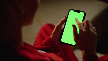 An over-the-shoulder view captures a woman using a smartphone with a green screen, potentially browsing or awaiting interaction.