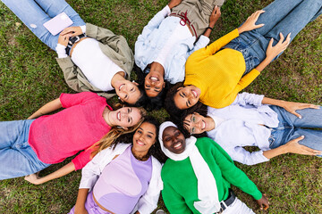 Portrait of diverse happy group of women looking at camera lying on grass at city park. Empowerment, people, female friendship and youth community concept.