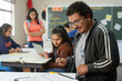 © Road Red Runner - A man is seen focusing and writing on a piece of paper while seated at a desk in a classroom setting.