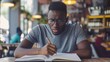 © buraratn - Focused millennial african american student in glasses making notes writing down information from book in cafe preparing for test or exam, young serious black man studying or working in coffee house