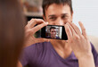© Mariusz S/peopleimages.com - Phone screen, photography and couple in house happy, bonding and having fun together. Smartphone, profile picture and woman with photo, app or romantic memory of husband while chilling in living room