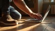 A man's hands are plugging in the power outlet adapter cord charger of a laptop computer on a wooden floor, illuminated by warm sunlight