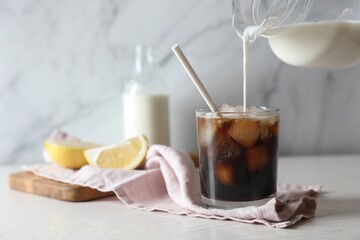 Wall Mural - Pouring milk into glass with refreshing iced coffee at white wooden table, closeup