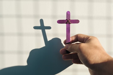 Wall Mural - Male hand holding purple wooden cross with shadow. Christianity, faith, holy week and lent season concept.