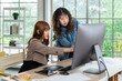 © wirojsid - Two young Asian female woman businessperson graphic designer working together, meeting and brainstorming, using computer in office, pointing at screen.