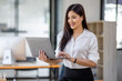 © David - Portrait of Asian beautiful joyful woman holding laptop doing finance and standing in the office