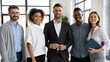 © fizkes - Happy colleagues at work. Aspiring young diverse coworkers smiling and looking at camera. Friendly staff members of multinational company standing close together for group photo in modern workspace