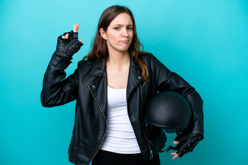 Wall Mural - Young caucasian woman with a motorcycle helmet isolated on blue background with fingers crossing and wishing the best