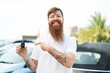 © luismolinero - Redhead man with beard holding car keys at outdoors and pointing it