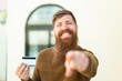 Redhead man with beard holding a credit card at outdoors points finger at you with a confident expression