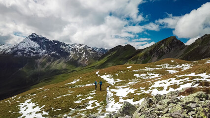 Wall Mural - Aerial view of hiker couple on alpine meadow looking at majestic mount Vorderer Geisslkopf in High Tauern National Park, Carinthia, Austria. Idyllic hiking trail Austrian Alps. Wanderlust paradise