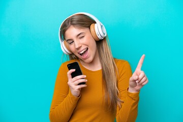 Wall Mural - Young caucasian woman isolated on blue background listening music with a mobile and singing