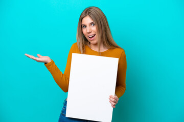 Wall Mural - Young caucasian woman isolated on blue background holding an empty placard with surprised expression