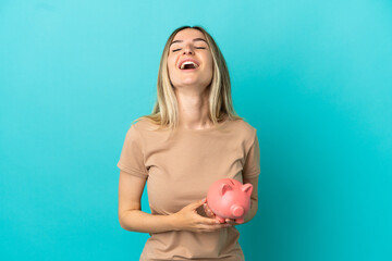 Wall Mural - Young woman holding a piggybank over isolated blue background laughing