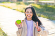 Young woman with an apple at outdoors smiling and showing victory sign