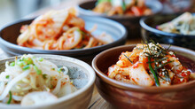 An Assortment Of Korean Banchan, Including Kimchi And Pickled Vegetables, Served In Stainless Steel Bowls.