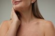 © New Africa - Mature woman touching her neck on grey background, closeup