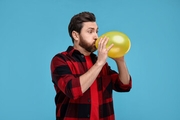 Wall Mural - Man inflating yellow balloon on light blue background