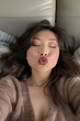 A selfie of a beautiful woman laying on a bed kissing with eyes closed