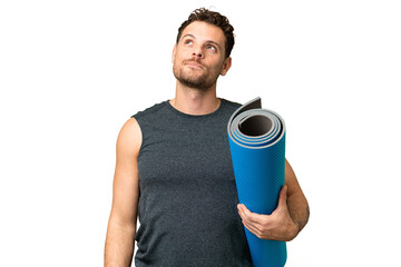 Wall Mural - Young sport man going to yoga classes while holding a mat over isolated chroma key background thinking an idea while looking up