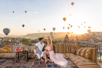 Beautiful morning in Cappadocia - a young couple and their romantic breakfast with an amazing background of flying balloons.