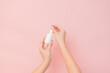 White bottle with serum lotion or essential oil (hyaluronic acid and collagen) in hands on pink background. Skin care cosmetics concept, beauty flyer
